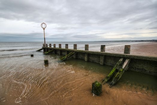 Old wooden groyne structure covered with green algae on Portobello beach during low tide with North sea in the backgroud shot on overcast day. Edinburgh, Scotland.