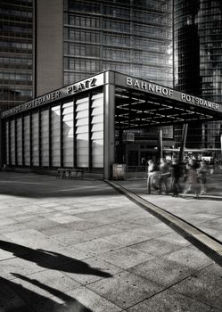 Berlin, Germany - September 15th, 2007: Wide black and white photo of Potsdamer platz bahnhof (underground tube) station entrance with people shadows in foreground.