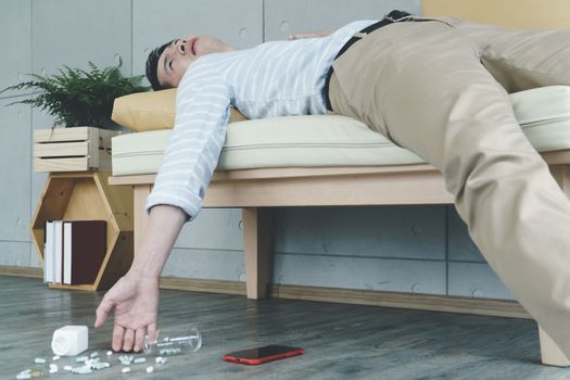 young Asian man suffers from a sudden heart attack. Lying unconscious in the apartment. Near his hand were several pills. And the smartphone is placed. Health, sick, and medical treatment concepts.