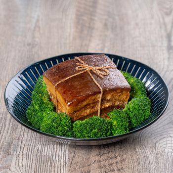 Dong Po Rou (Dongpo pork meat) in a beautiful blue plate with green broccoli vegetable, traditional festive food for Chinese new year cuisine meal, close up.