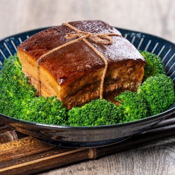 Dong Po Rou (Dongpo pork meat) in a beautiful blue plate with green broccoli vegetable, traditional festive food for Chinese new year cuisine meal, close up.