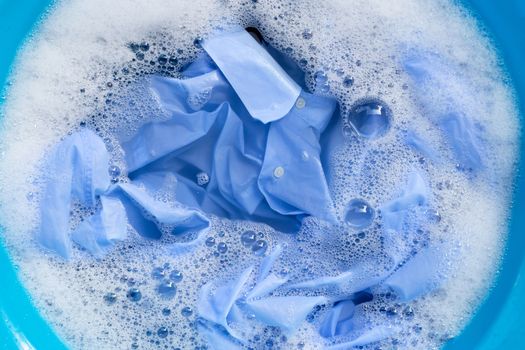 Top view of blue shirt soak in powder detergent water dissolution. Laundry concept