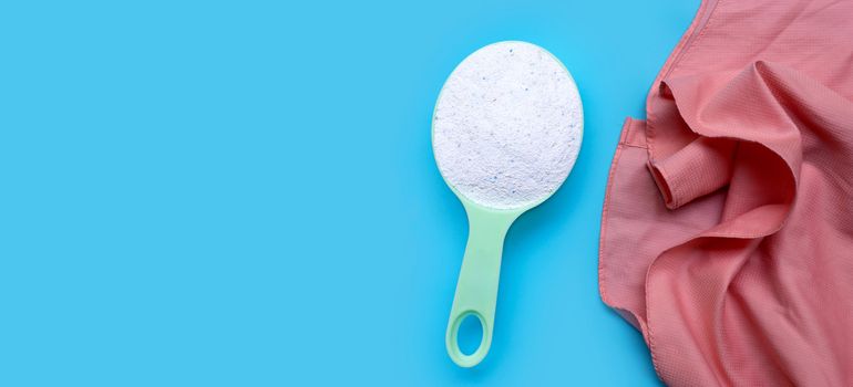 Detergent powder in measuring spoon with pink cloth on blue background. Laundry concept.