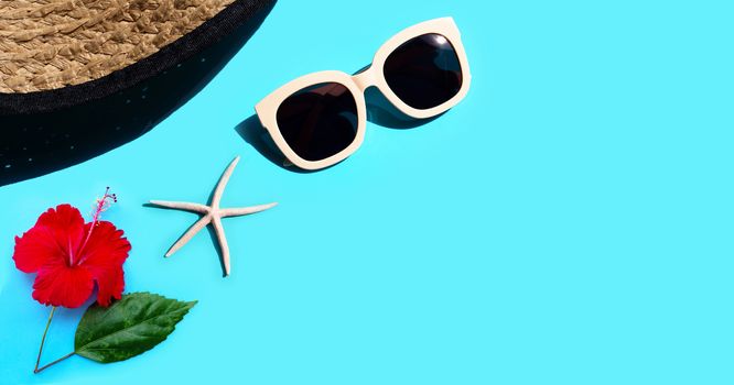 Summer hat with sunglasses, hibiscus flower and starfish on blue background. Enjoy holiday concept. Copy space