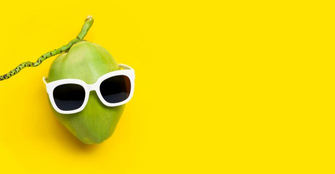 Coconut with sunglasses on yellow background. Copy space