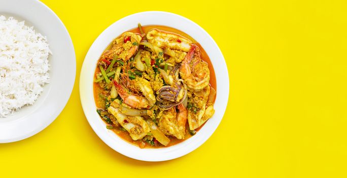 Fried seafood with curry powder with dish of rice on yellow background.