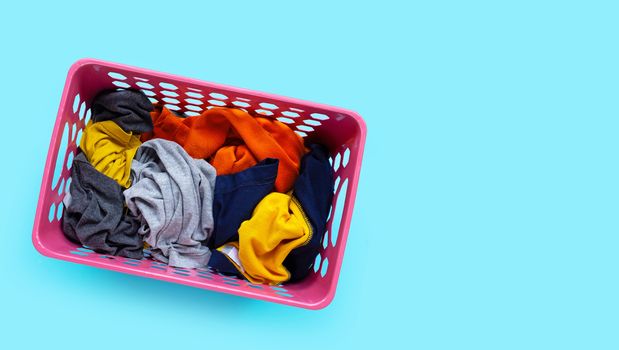 Clothes in pink plastic laundry basket on blue background. Laundry concept