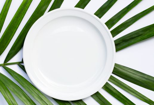Empty white ceramic plate on tropical palm leaves on white background. Top view