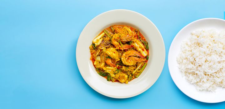 Fried seafood with curry powder with dish of rice on blue background.