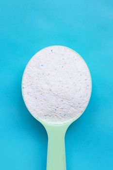 Detergent powder in measuring spoon on blue background. Laundry concept.