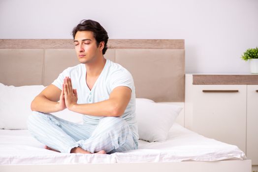 Young man doing yoga in bed