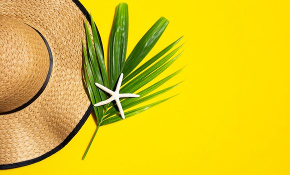 Summer hat with starfish on tropical palm leaves with  on yellow background. Top view