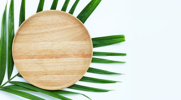 Empty wooden plate on tropical palm leaves on white background.