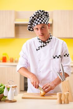 Young professional cook preparing salad at kitchen
