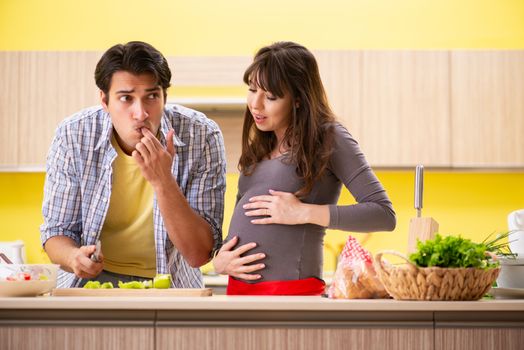 Man and pregnant woman preparing salad in kitchen 