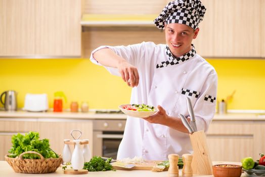 Young professional cook preparing salad at kitchen