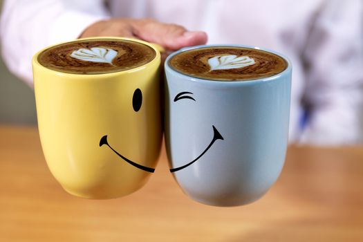 Close up Hand businessman hold coffee cups with smle face background. Hand man hold yellow and blue coffee cups with heart shape creamy and smile background.