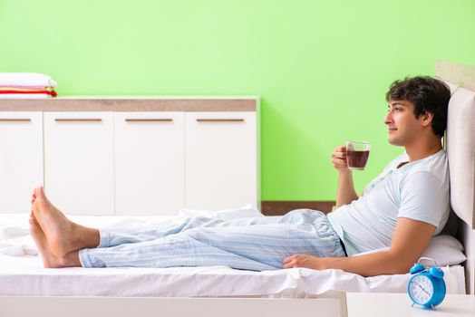 Young handsome man drinking coffee in the bed 