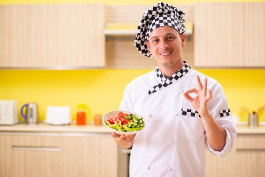 Young professional cook preparing salad at kitchen