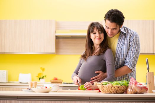 Man and pregnant woman preparing salad in kitchen 