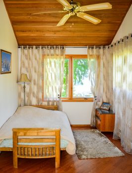 Small lightful bedroom with curtains on windows and rug on the floor
