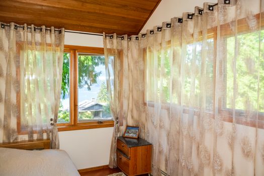 Wide windows and curtains in small bedroom with ocean bay view