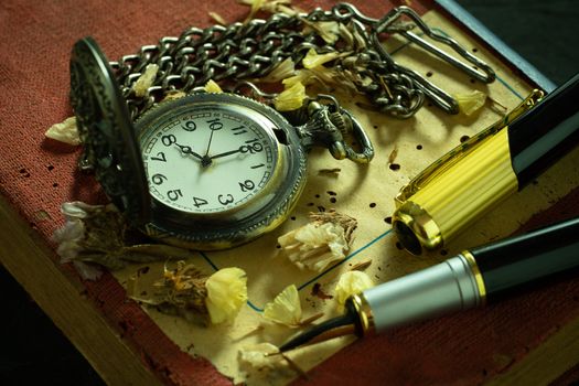 Vintage pocket watch and brass pen on old book. At 8 o'clock in morning. Education and vintage style concept.