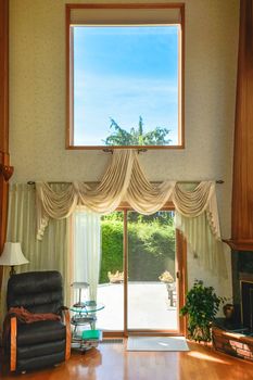 High ceiling beautiful living room interior with hardwood floor. Leather chair and fireplace beside the patio door