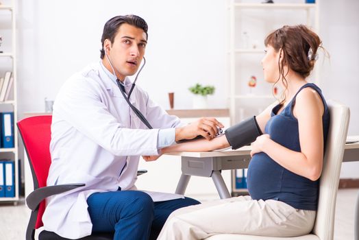 Young doctor checking pregnant woman's blood pressure