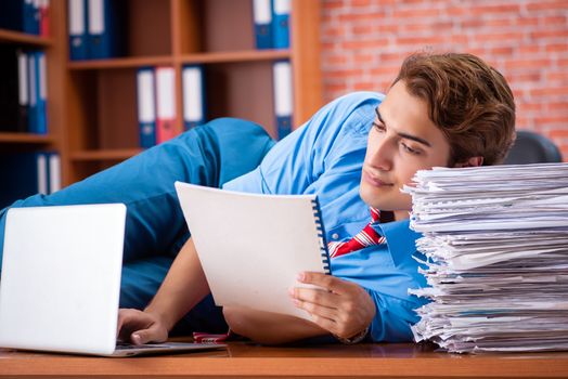 Young employee with excessive work sitting at the office 