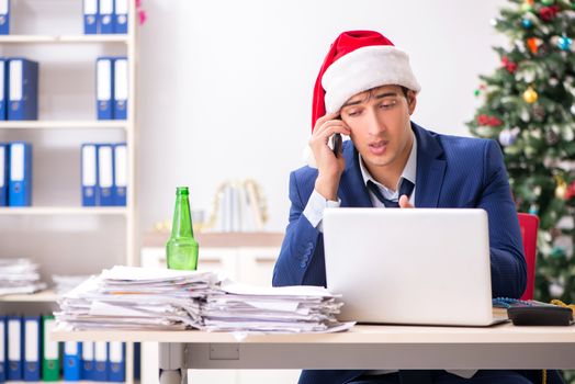 Young handsome employee celebrating Christmas at workplace 