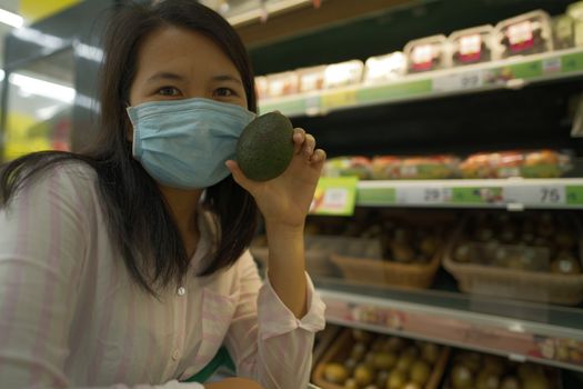 Shopping woman holding avocado fruit in a mall wearing a coronavirus mask select focus