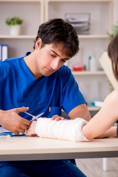 Young woman with bandaged arm visiting male doctor traumotologist 