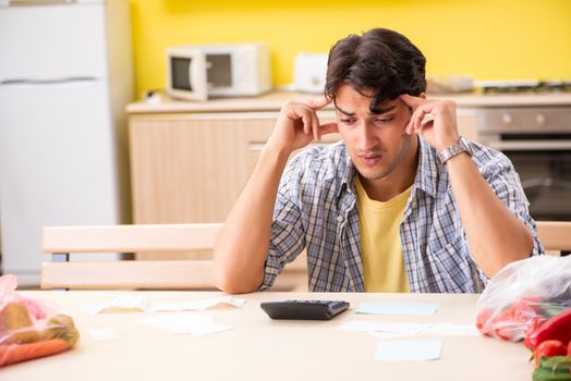 Young man calculating expences for vegetables in kitchen 
