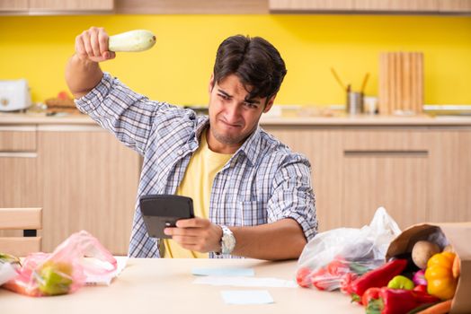 Young man calculating expences for vegetables in kitchen 