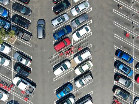 Aerial top view of parking lot at shopping mall with varieties of colored vehicles. People walking to their car and trying to park.