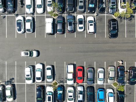 Aerial top view of parking lot at shopping mall with varieties of colored vehicles. People walking to their car and trying to park.