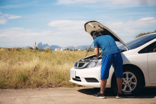 Young man is checking cars on a road in the countryside.