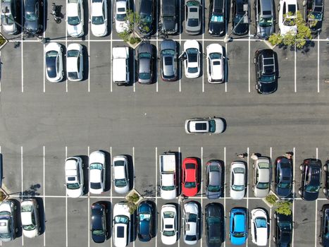 Aerial top view of parking lot at shopping mall with varieties of colored vehicles. People walking to their car and trying to park.