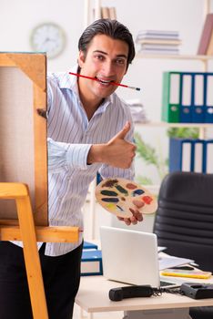 Young handsome employee enjoying painting at the office 