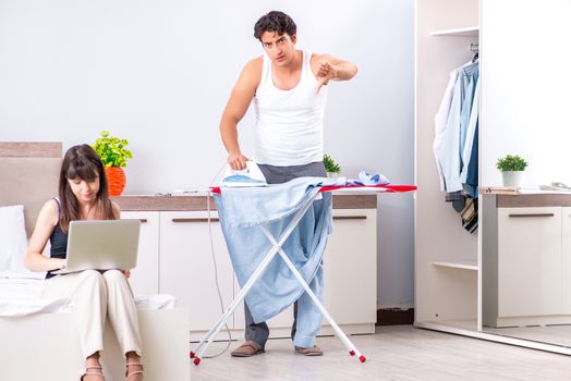 Man ironing, his lazy wife sitting 