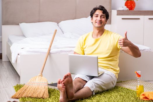 Young handsome man cleaning the bedroom and sitting at the computer