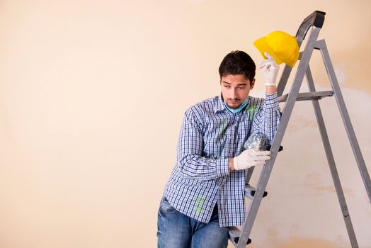 Young contractor sanding wall down with sandpaper 
