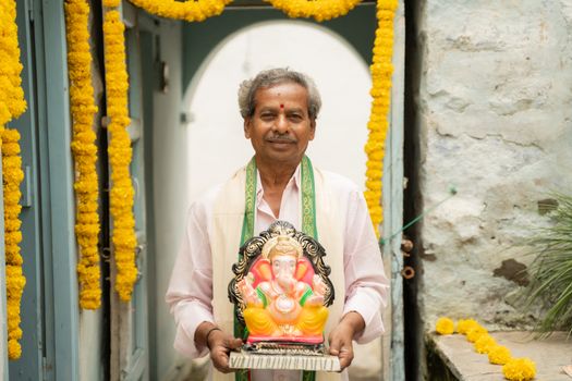 happy Elder man with Ganesha Idol coming home during ganesha or vinayaka Chaturthi festival - Concept of indian religious festival celebration