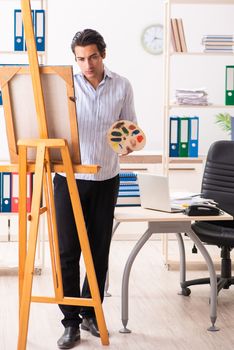 Young handsome employee enjoying painting at the office 