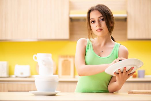 Young woman cleaning and washing dishes in kitchen
