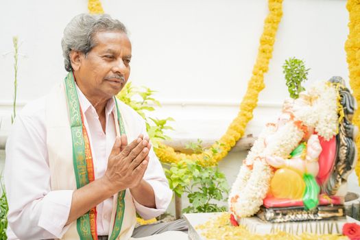 Elder man offering Bhajan or hymn in front of Lord Ganesha Idol during Ganesha or vinayaka Chaturthi festvial ceremony at home