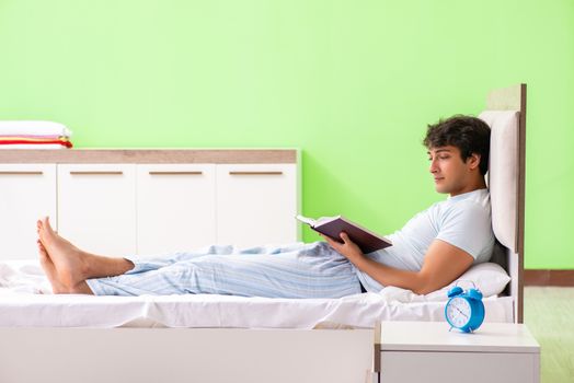 Young handsome student reading book in the bed 