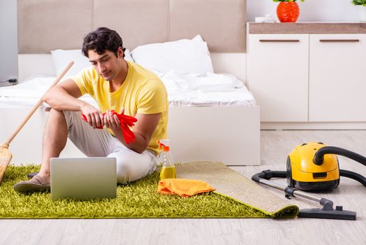 Young handsome man cleaning the bedroom and sitting at the computer
