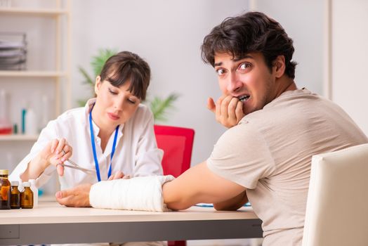 Young man with bandaged arm visiting female doctor traumatologist